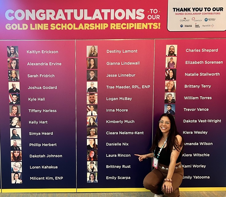 A woman points at a name on a large poster featuring photos and names underneath the words "Congratulations to our Gold Line Scholarship Recipients!" 